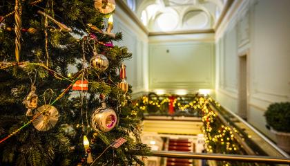 Joulukuusi on koristeltu runsaasti, taustalla näkyy lisää jouluvaloja kiinnitettynä yläkerran kaiteeseen.