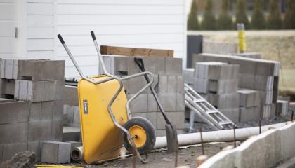 Keltaiset kottikärryt ja lapio harkkotiilien joukossa rakennustyömaalla. 