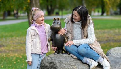 Vaaleatukkainen tyttö ja tummatukkainen nainen muumipatsaan ympärillä.