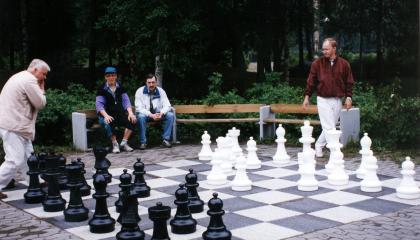 Iso shakkilauta maassa, ympärillä pelaajia.