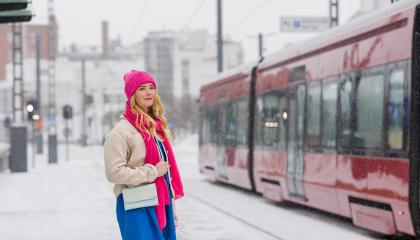 Punapipoinen tyttö odottaa ratikkaa talvisessa säässä ratikkaa.