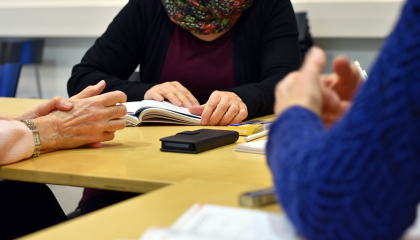 Kolmen henkilön kädet pöydällä. Pöydällä on opiskelutarvikkeita ja puhelin.