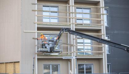 Rakenteilla olevan kerrostalon edustalla työntekijä nosturissa talon parvekkeen luona tekemässä työtään. 