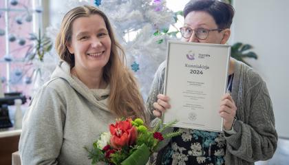 Kaksi henkilöä, joista toinen pitää käsissään kukkakimppua ja toinen kunniakirjaa