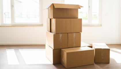Useita pahvisia muuttolaatikoita päällekkäin tyhjässä huoneessa jossa kaksi ikkunaa ulos.