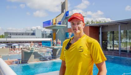 Maauimalan kesätyöntekijä seisoo maauimalassa taustallaan altaat ja hyppytorni.