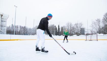 Etualalla seisova pelaaja on syöttämässä kiekkoa maalin lähellä seisovalle toiselle pelaajalle.