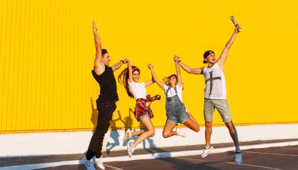 Kuvassa neljä henkilöä hyppäämässä ilmaan keltaisen seinän edessä
