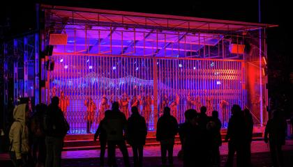 Kulttuuriosuuskunta Uulun kuorot esittävät yleisölle Laikunlavan verkkoportista roikkuen Urbaani katedraali -teosta sinipunaisessa valalaistuksessa.