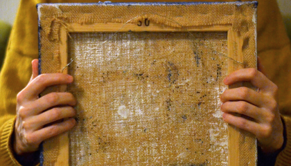 Ihminen pitää sylissään nurinpäin olevaa maalausta.