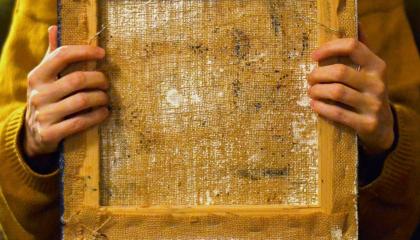 Keltapaitainen henkilö pitää sylissään vanhaa taulun kehystä, josta näkyy teoksen tausta.