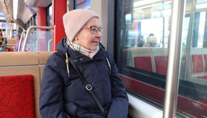 Vanhempi henkilö matkustaa ratikassa, katselee ulos.