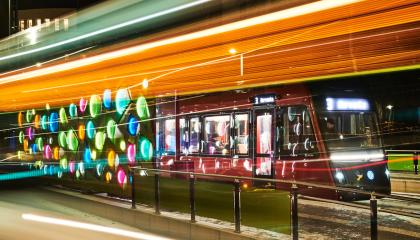 Kuvassa värikäs valotaideteos pysäkillä ja raitiotievaunu sen takana.