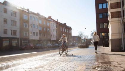 Pyöräilija, jalankulkija ja harjaustraktori kadulla.