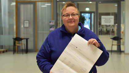 Henkilö seisoo aulassa. Hänellä on kädessään juliste.