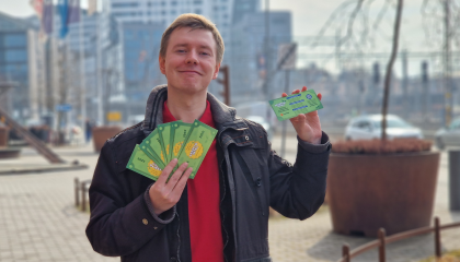 Henkilö seisoo pihalla ja esittelee kameralle vihreää Kesätyöseteliä. Taustalla näkyy korkeita kerrostaloja.