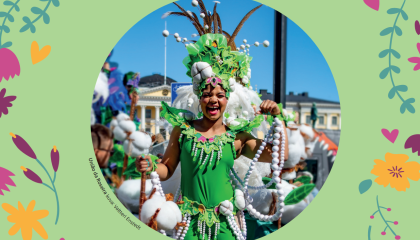 Sambaajalla on päällään vihreä karnevaaliasu ja hän hymyilee tanssiessaan.