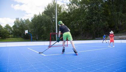 Kolme eri-ikäistä pelaajaa pelaa mailojen kanssa sinipohjaisella kentällä ulkona.