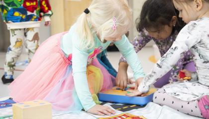 Kolme pientä tyttöä leikkii lattialla.