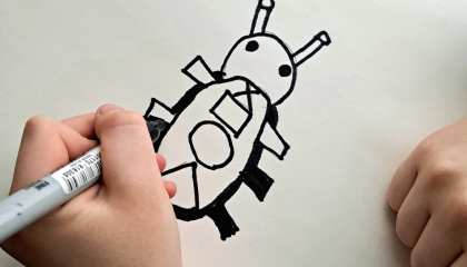 Lapsen kädessä mustan värinen tussi ja lapsi piirtää koppakuoriaisen näköistä ötökkää valkoiselle paperille.