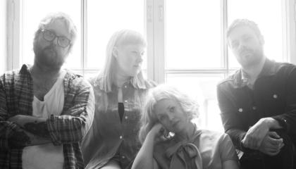 Nelihenkinen yhtye istuu ikkunan edessä, ikkunasta tulee kirkas valo.