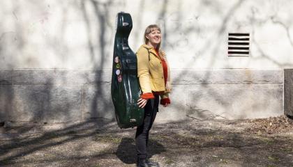 Kielo-Kristiina Kärkkäinen seisoo ulkona sellokotelo selässään.