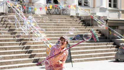 Punaisiin pukeutunut nainen pitää käsissään värikästä harjanvartta ja ihailee saippuakuplia.