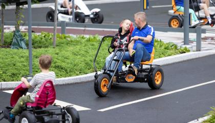Liikennepuistossa lapsia polkee polkuautolla, keskellä rinnakkain ajettava polkuauto, jossa lapsi ja aikuinen.