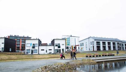 Ihmisiä kävelemässä lammen rannalla asuinalueella.