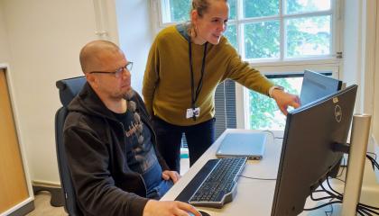 Kaksi kaupungin asiantuntijaa tutkimassa tietokoneelta Power BI -raporttia. Toinen istuu tuolilla ja toinen näyttää kädellään jotain tietokoneen ruudulla näkyvää tietoa.