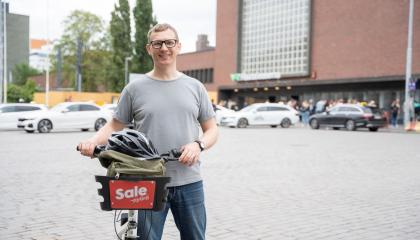 Henkilö rautatieaseman edustalla kaupunkipyörän kanssa.