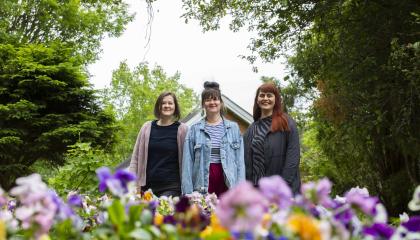  Liisa Aholainen, Janina Ahlfors ja Mirjam Larinkari katsovat kameraan kukkapenkkien takaa.
