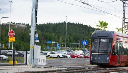 Ratikka saapuu pysäkillä, taustalla autoja parkissa liityntäpysäköintialueella.