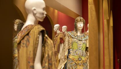 Costumes from the Roman Opera displayed in a museum. Dresses have shades of gold and they have been put on white mannequin dolls.