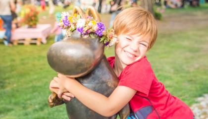 Poika halaa kukkaseppelöityä Muumipeikkopatsasta Sorsapuistossa Tampereella.