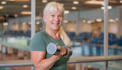 Hymyilevä vanhempi nainen kuntoilee kuntosalilla.