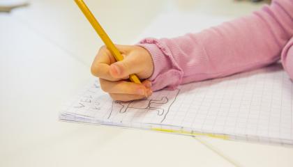 Pienen lapsen käsi piirtämässä lyijykynällä vihkoon