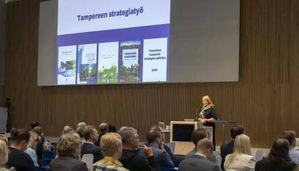 Yleisö katsomossa istumassa ja kuuntelemassa puhujaa.