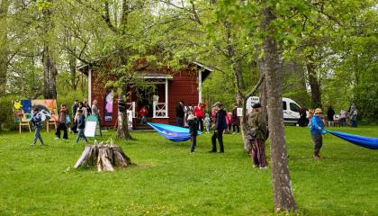 Ihmisiä vihreässä puistossa, jossa on värikkäitä taideteoksia. Osa ripustaa riippumattoja. 