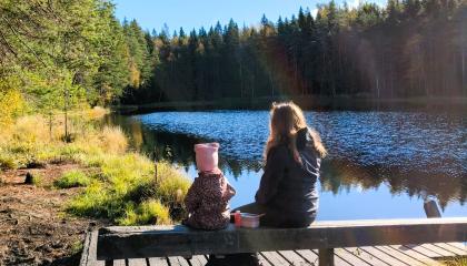 Lapsi ja nainen istuvat auringossa laiturin penkillä katsellen järvelle.