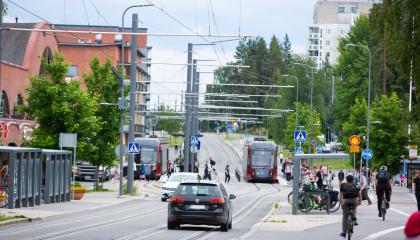 Henkilöautoja, ratikoita, pyöräilijöitä ja kävelijöitä Hervannan keskustassa.