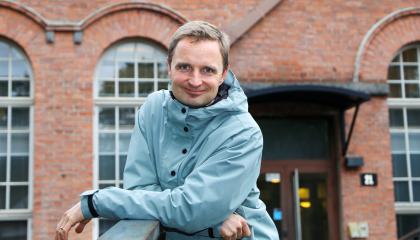 Mikko katsoo suoraan kameraan taustallaan Frenckellin punatiilinen rakennus.