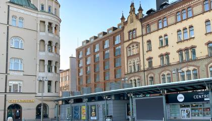 Kuvassa vanhoja kerrostaloja, keskellä uuden rakennuksen havainnekuva, etualalla torin kioski.