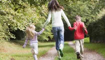 Aikuinen ja kaksi lasta juoksevat käsi kädessä kesäisellä metsäpolulla.