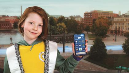 Poika seisoo Tampere-maiseman edessä ja näyttää kameralle Tampere.Finland -sovellusta.