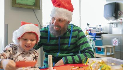 Pieni tyttö ja mies askartelevat korttia iloisina tonttulakit päässään.