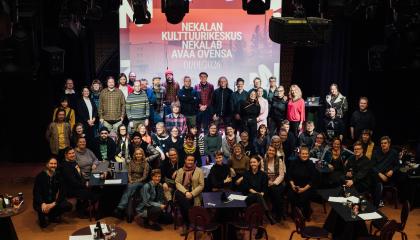 Suuri ryhmä ihmisiä poseeraa yhteiskuvassa. Taustalla valotaulu, jossa lukee &quot;Nekalan kulttuurikeskus Nekalab avaa ovensa 1.1.2026&quot;.