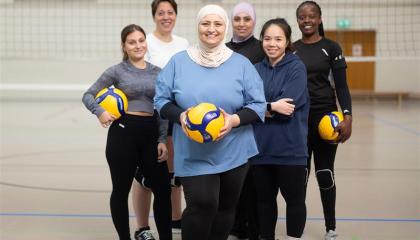 Kuusi naista lentopallokentällä ryhmäkuvassa. Kolmella heistä on lentopallo kädessä