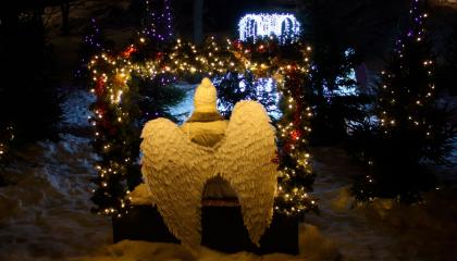 Enkelisiipiin pukeutunut hahmo istuu selin kameraan lumisessa joulukuusipuistossa.