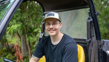 Henkilö istuu työkoneen kyydissä ja nojaa toisella kädellään rattiin.